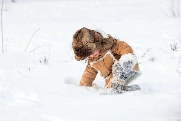 A boy in winter Russian folk clothes crawls through snowdrifts.Winter picture — Foto Stock