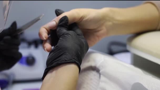 Мастер маникюра в черных одноразовых перчатках исправляет ногти — стоковое видео