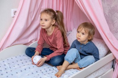 Bir kız ve bir oğlan küp şeklinde bir projektörle bir yatakta oturuyorlar.