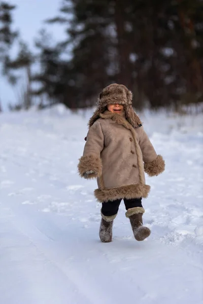 Un bambino in pelliccia invernale, cappello e stivali di feltro in una foresta innevata — Foto Stock