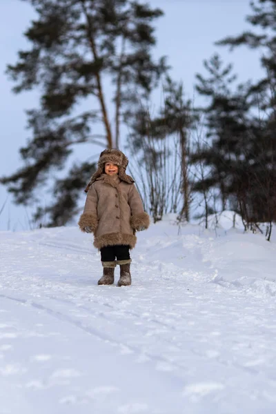 Un bambino in pelliccia invernale, cappello e stivali di feltro in una foresta innevata — Foto Stock