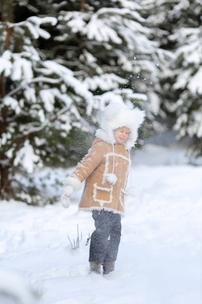Una ragazza in un cappello di pelliccia divertente e cappotto di pelle di pecora sta giocando in una foresta innevata — Foto Stock