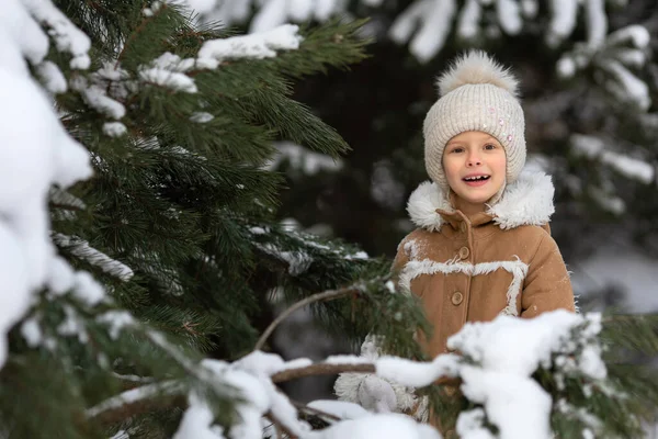 Una ragazza in un cappello invernale e cappotto di pelle di pecora sta giocando in una foresta innevata — Foto Stock