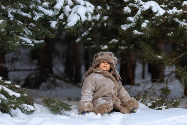 Un ragazzo carino in pelliccia e un cappello con paraorecchie cammina in inverno — Foto Stock