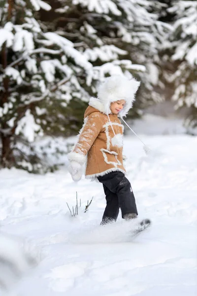 Una ragazza in un cappello di pelliccia divertente e cappotto di pelle di pecora sta giocando in una foresta innevata — Foto Stock