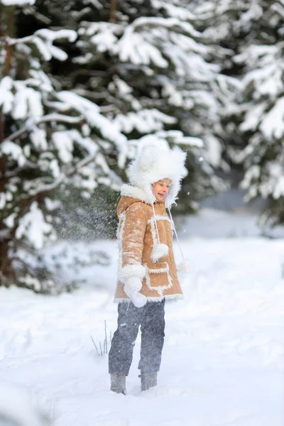 Una ragazza in un cappello di pelliccia divertente e cappotto di pelle di pecora sta giocando in una foresta innevata — Foto Stock