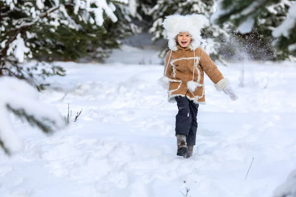 Девушка в меховой шапке и шубе играет в снежном лесу — стоковое фото