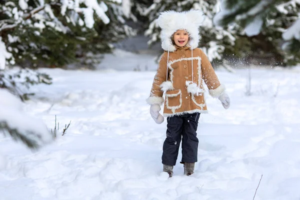 Девушка в меховой шапке и шубе играет в снежном лесу — стоковое фото