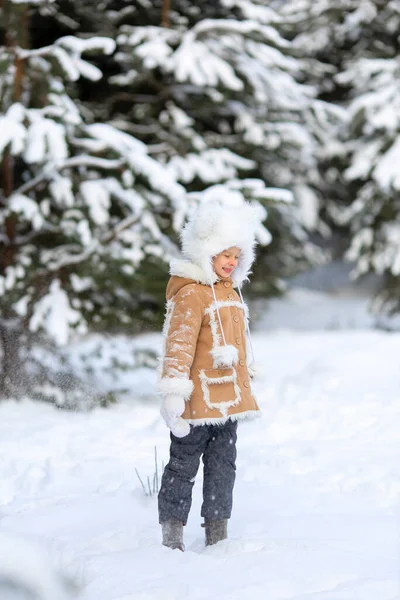 Una ragazza in un cappello di pelliccia divertente e cappotto di pelle di pecora sta giocando in una foresta innevata — Foto Stock