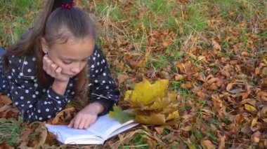 Sarı sonbahar yaprakları üzerine uzanmış kitap okuyan kız.