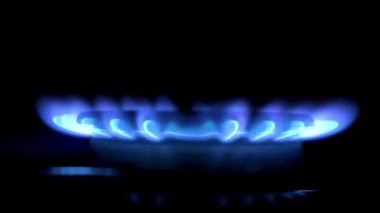 Gaz ocağı açık, geceleri mavi alevle parlıyor. Yakın plan. Siyah arka planda gaz sobası. Doğal gaz yanıyor..