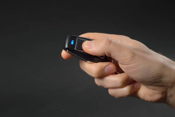 Unlocking the car by the car\'s key remote control. Man hand pressing the button of the car key. Black background. Close-up.