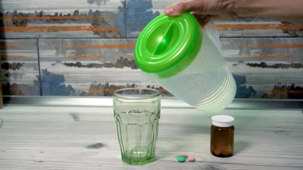 一个人把水壶里的水倒入杯子里 然后吃药 药物治疗 定期摄入药物 多种维生素 生物补充剂 — 图库视频影像