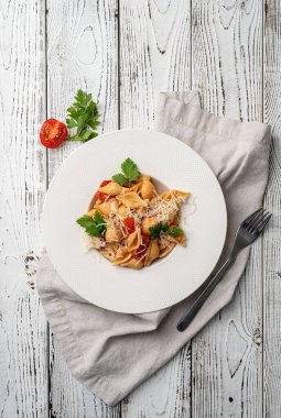 Kiraz domatesli konşiglionili makarna, peynir ve maydanoz beyaz tabakta ahşap arka planda, üst görünüm kopya alanı