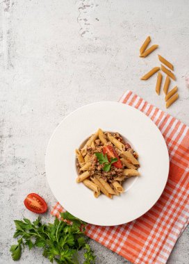 Çeri domatesli bolonez soslu makarna, beton arka planda beyaz tabakta et ve maydanoz, üst görünüm kopya alanı