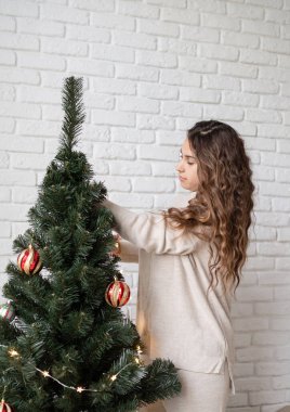 Mutlu Noeller ve mutlu yıllar. Genç ve çekici bir kadın Noel ağacını peri ışıklarıyla süslüyor.
