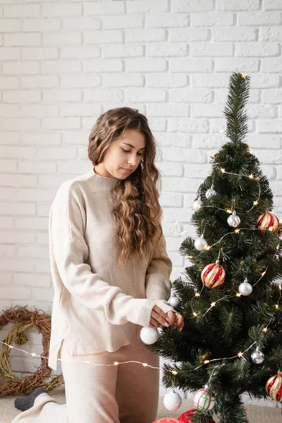 Genç ve çekici bir kadın Noel ağacını peri ışıklarıyla süslüyor. — Stok fotoğraf