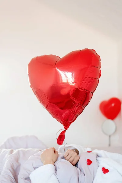 Молодая блондинка лежит в постели с праздничным подарком и красными конфетти — стоковое фото