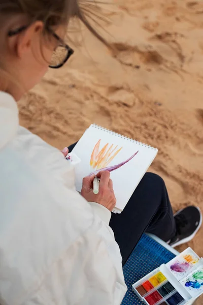 Молодая женщина художник рисует или делает путешествия эскизы с использованием акварели на берегу моря — стоковое фото