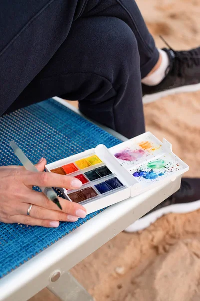 Närbild av akvarell palett, ung kvinna konstnär måla eller göra resor skisser med hjälp av akvarell vid havet — Stockfoto