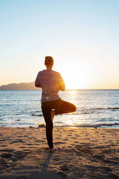 Молода здорова жінка практикує йогу на пляжі на сході сонця — стокове фото