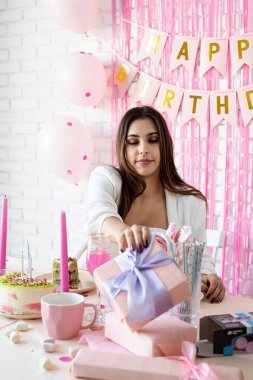 Doğum günü partisi. Doğum günü masaları. Beyaz parti kıyafetleri içinde çekici bir kadın doğum günü masasını kek, pasta, badem kurabiyesi ve diğer şekerlerle hazırlıyor.