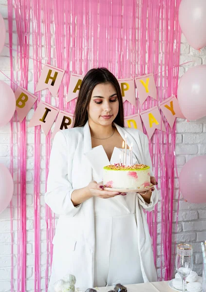 Doğum günü partisi. Doğum günü masaları. Beyaz parti kıyafetleri içinde çekici bir kadın doğum günü masasını kek, pasta, badem kurabiyesi ve diğer şekerlerle hazırlıyor.