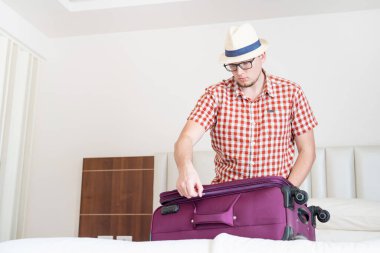 Tatilde. Yazlık şapkalı yakışıklı beyaz adam seyahat için bavulunu hazırlıyor.