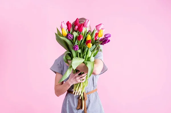 International Women's Day. pretty charming brunette young woman dressed yellow clothes holding tulip bunch isolated pink color background