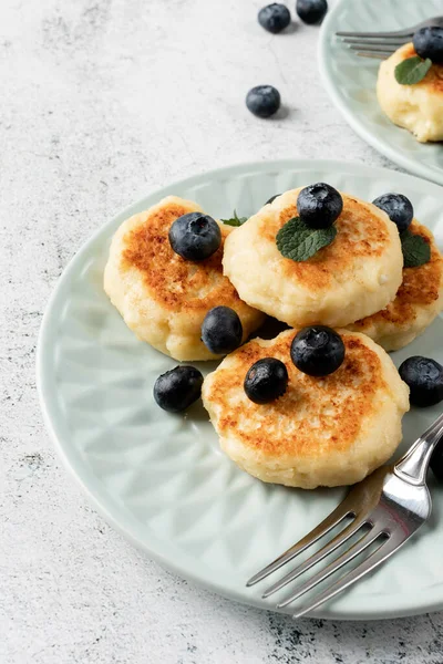 stock image Cottage cheese fritters with blueberries on ceramic blue plate on concrete background. Healthy calcium breakfast, lunch or snack. Traditional russian food. Close up