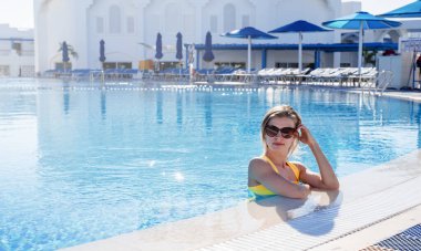 Tatil ve turizm. Güneş gözlüğü takan genç sarışın kadın bilardoda eğleniyor. Havuzda genç bir kadının portresi.
