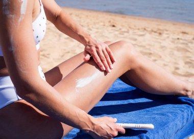 Güneş koruma kozmetik ürünleri. Genç, beyaz bir kadın sahilde güneş kremi sürüyor.