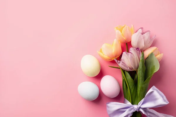 Home decoration for holiday. easter background with eggs and tulips on pink backdrop, top view flat lay