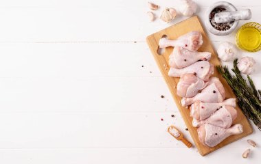 Kesme tahtasında derisi olan dilimlenmiş tavuk bacağı. Beyaz ahşap arka plan. Üst görünüm