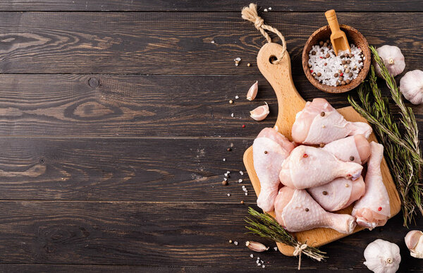 Sliced chicken legs with skin on a cutting board. Dark wooden background. Top view