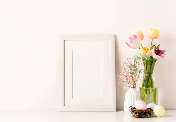 Mockup con una cornice bianca tulipani primaverili in vaso, gypsophila e uova color pastello su sfondo chiaro — Foto Stock