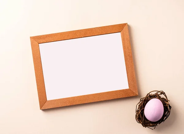 Drewniana rama z kolorowym jajem wielkanocnym płaska leżała na beżowym tle — Zdjęcie stockowe