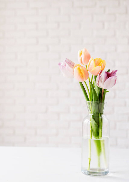 Pastel colored tulips in vase on white brick wall background