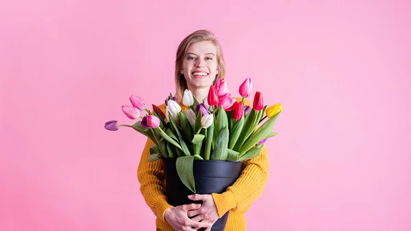 International Women\'s Day. pretty charming brunette young woman dressed yellow clothes holding tulip bunch isolated pink color background