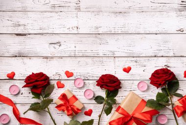 Romantic Valentine's day flat lay with copy space for text. Romantic composition of red roses, gifts and candles top view on white wooden background. Valentines day greeting card