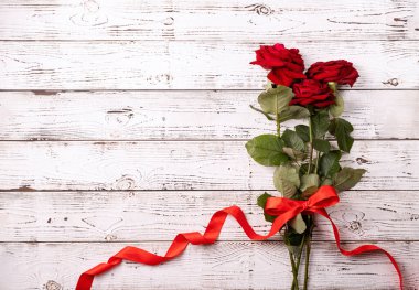 Romantic Valentine's day flat lay with copy space for text. Red roses bouquet with copy space top view on white wooden background. Valentines day greeting card