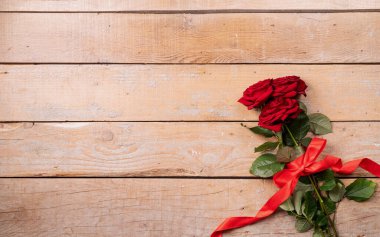 Romantic Valentine's day flat lay with copy space for text. Red roses bouquet with copy space top view on wooden background. Valentines day greeting card