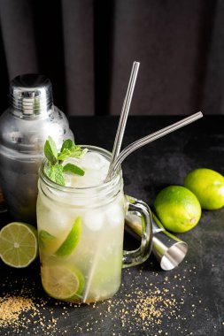 fresh summer caipirinha cocktail on a black background with green fruit lime on table