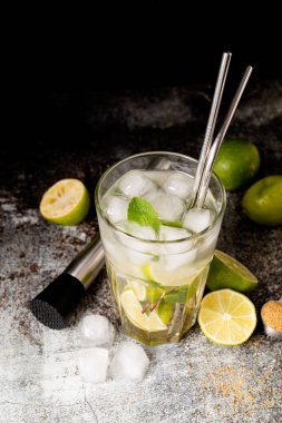 fresh summer caipirinha cocktail on concrete background with green fruit lime on table