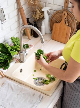 Preparing healthy foods. Healthy eating and dieting. Young smiling woman in home clothes washing spinash in the kitchen