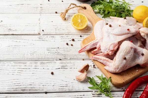 Sliced chicken wings with skin on a cutting board. White wooden background with copy space