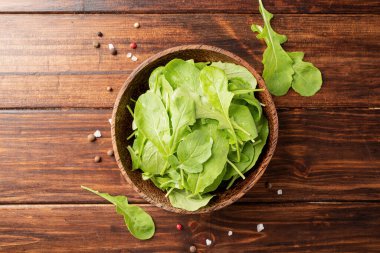 Healthy eating and dieting. Fresh arugula leaves in brown coconut bowl on wooden background top view, flat lay