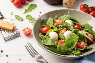 Healthy eating and dieting. Fresh salad with arugula, cherry tomatoes, mozzarella cheese and hard cheese on white wooden background. Top view