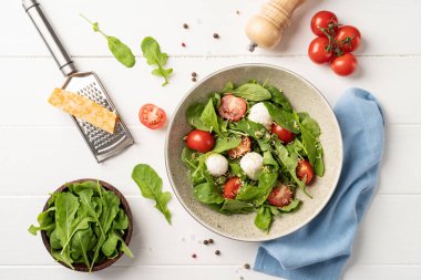 Healthy eating and dieting. Fresh salad with arugula, cherry tomatoes, mozzarella cheese and hard cheese on white wooden background. Top view