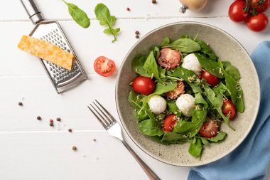 Healthy eating and dieting. Fresh salad with arugula, cherry tomatoes, mozzarella cheese and hard cheese on white wooden background. Top view